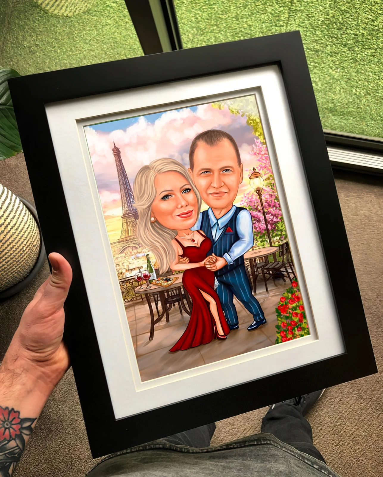 A couple&rsquo;s caricature with the Eiffel Tower behind them, in a wide black frame with a mount.